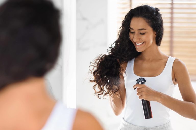 une femme qui applique du hair spray sur ses cheveux bouclés